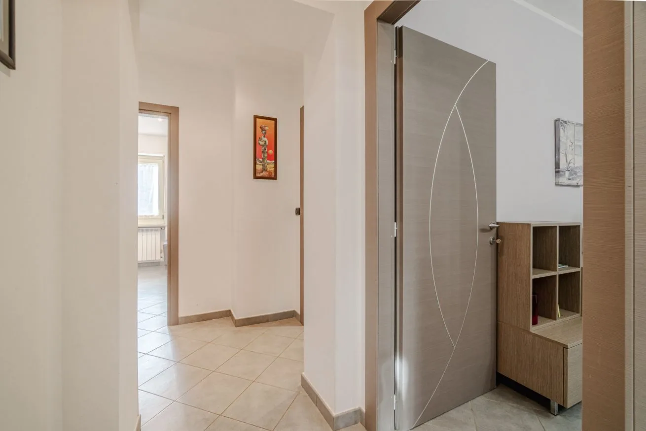 Un pasillo con baldosas conduce a una habitación junto a una puerta gris abierta.