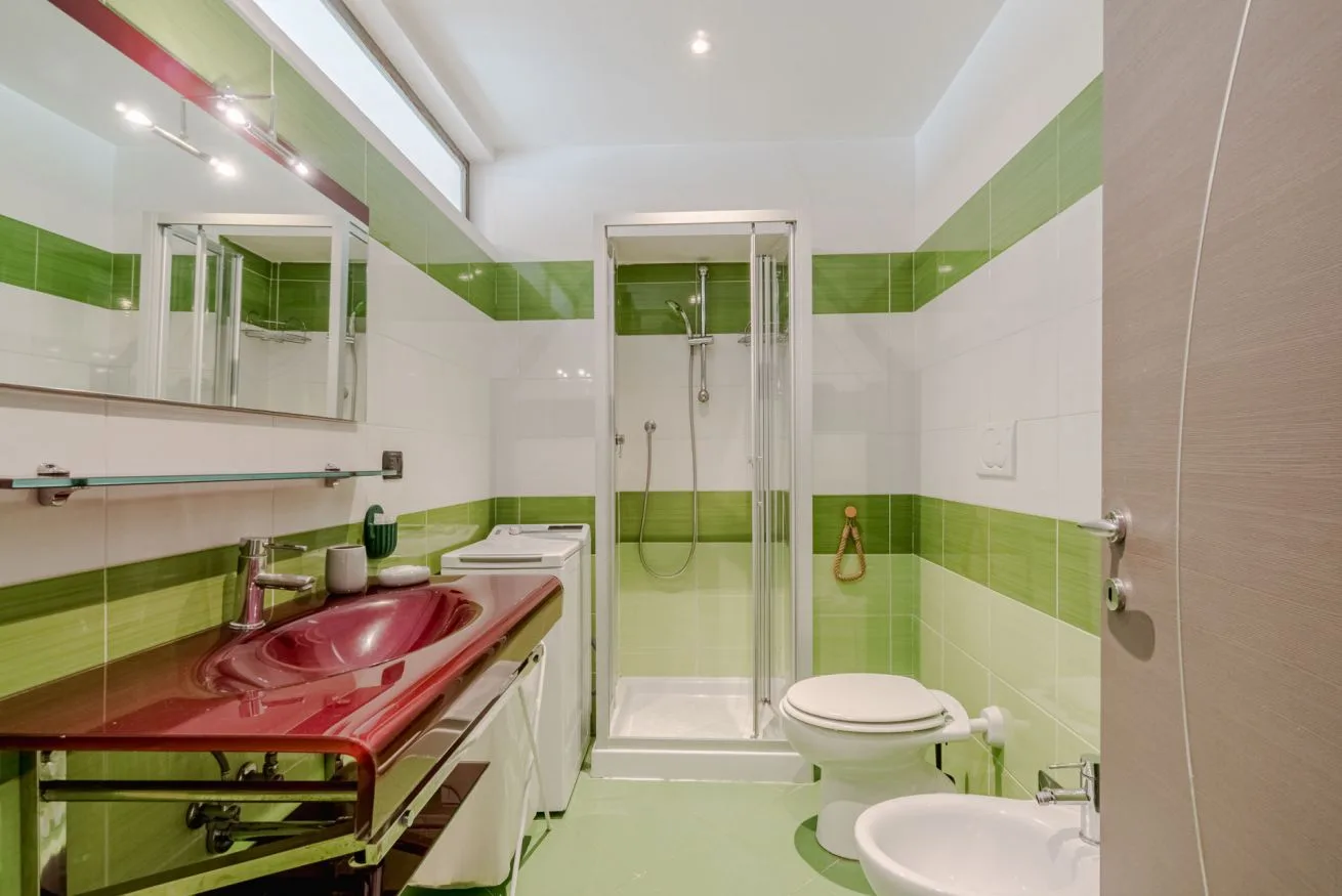 Un baño de azulejos con una ducha de vidrio y una encimera roja con lavabo.