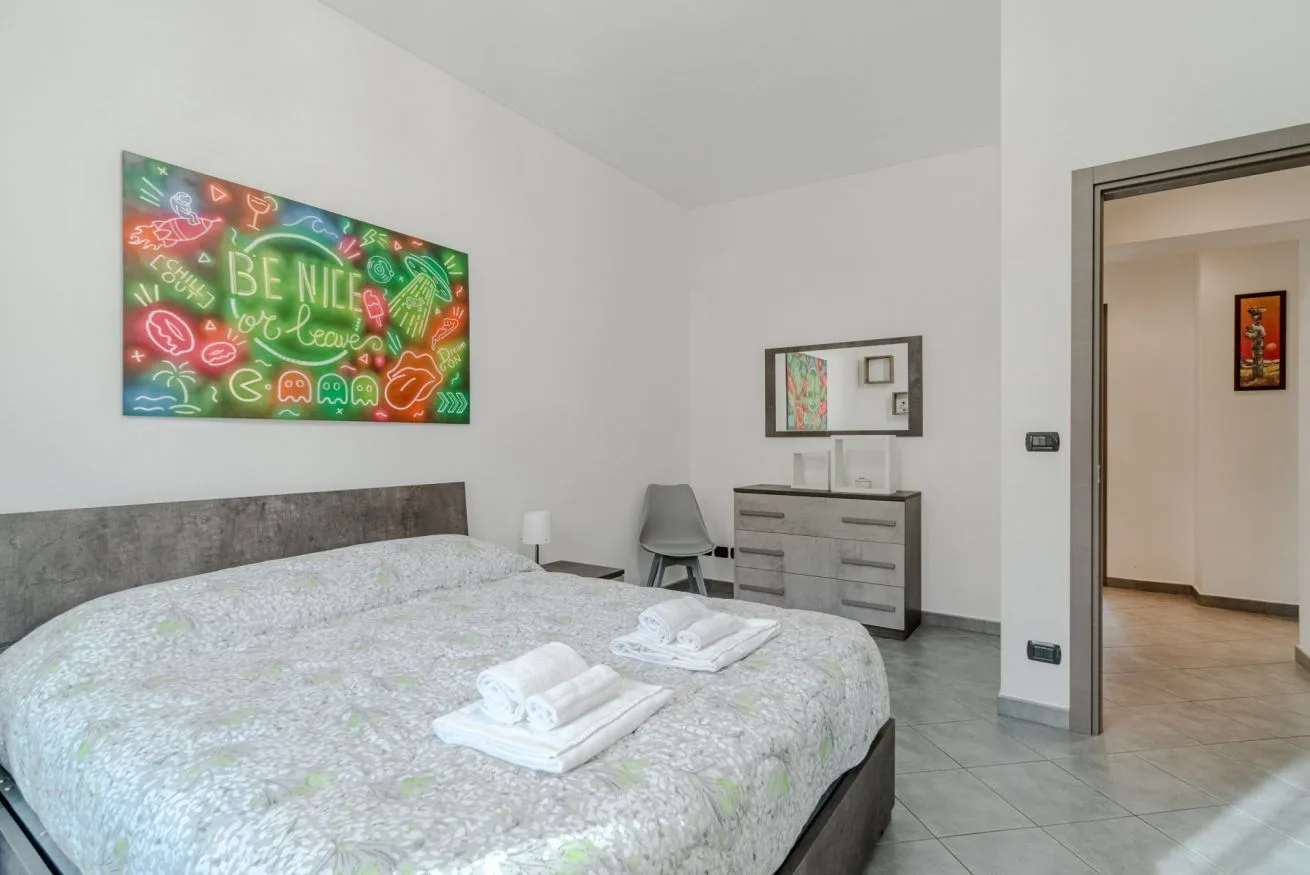 Un dormitorio con una cama bien arreglada y arte colorido en la pared.