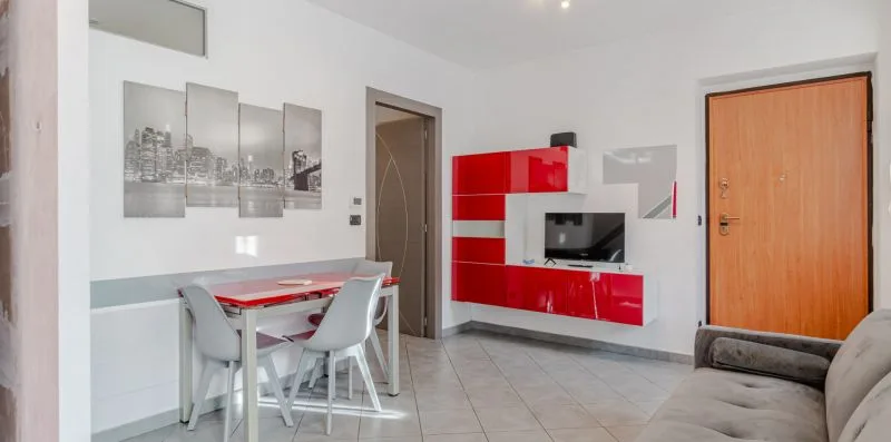 Una luminosa sala de estar y comedor con un mueble rojo para televisión y una mesa de comedor.