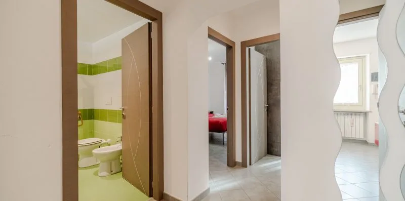Un pasillo conecta habitaciones con entradas a un baño de azulejos verdes y un dormitorio.
