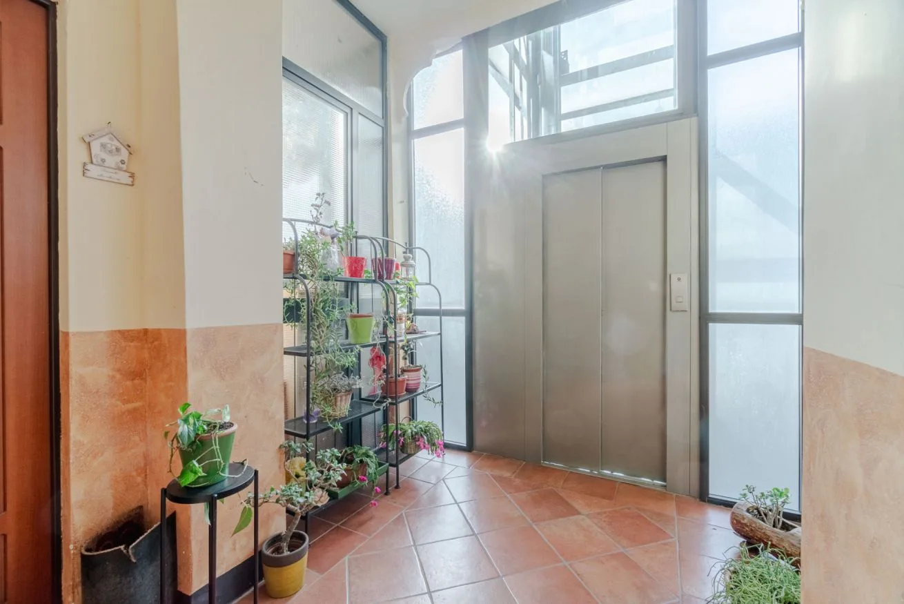 Una entrada luminosa con suelo de baldosas, un ascensor y plantas en macetas.
