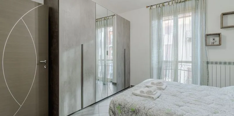 Un dormitorio con una cama, un armario con espejo y una ventana con cortinas translúcidas.