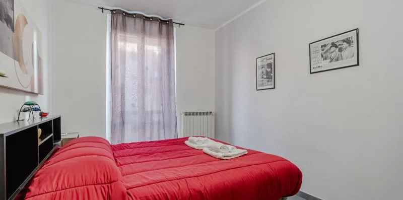 Un dormitorio con una cama roja, una ventana y cuadros en las paredes.