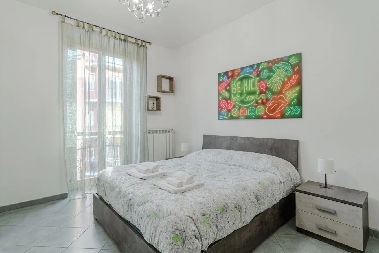Un dormitorio con una cama grande, cortinas claras y arte colorido en la pared.