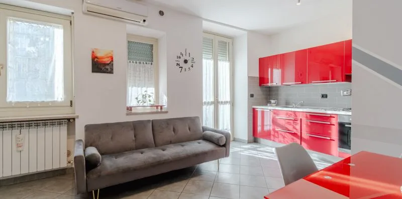 Una sala de estar con un sofá gris junto a una cocina roja.