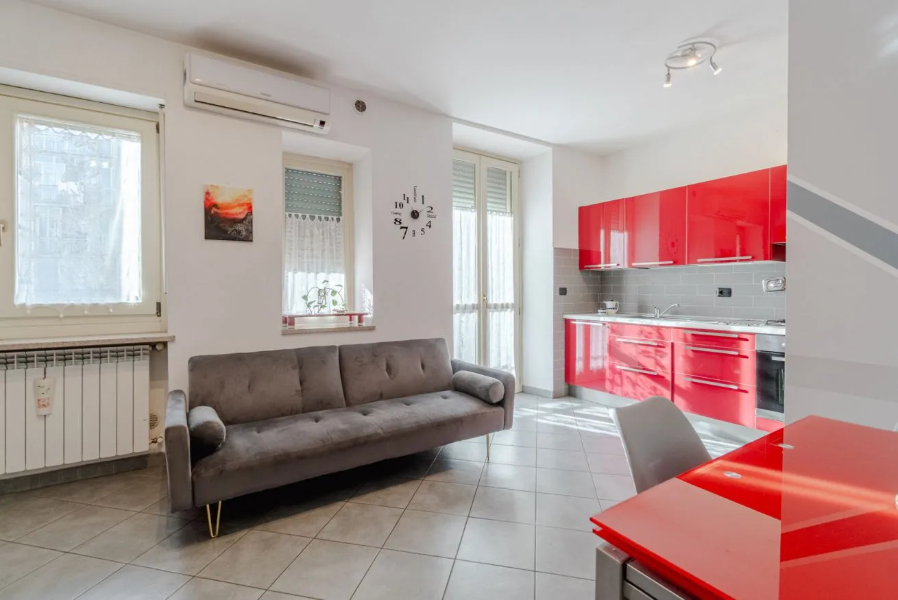 Una sala de estar con un sofá gris junto a una cocina roja.