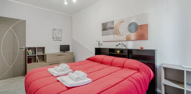 Un dormitorio con una cama roja, toallas dobladas y arte abstracto en la pared.