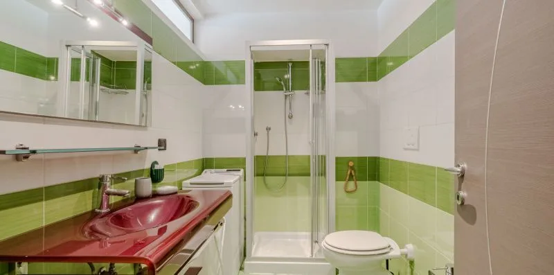 Un baño alicatado con lavabo rojo, inodoro y ducha de vidrio.