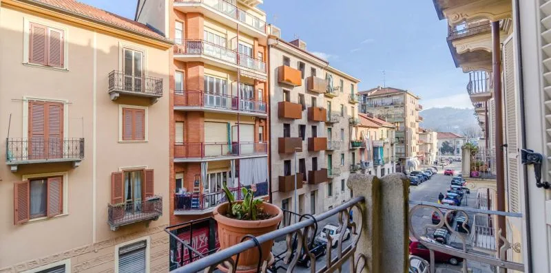 Una calle urbana vista desde un balcón, con edificios de apartamentos y coches aparcados.