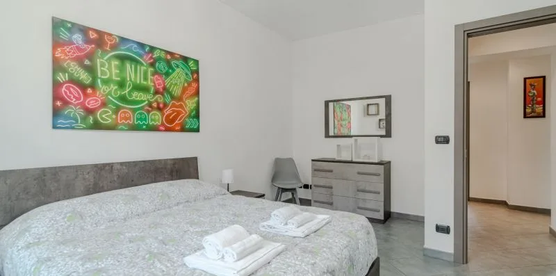 Un dormitorio con una cama, toallas dobladas y arte colorido en la pared.