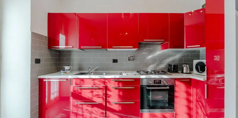 Una cocina moderna con gabinetes rojos brillantes, azulejos grises y electrodomésticos integrados.