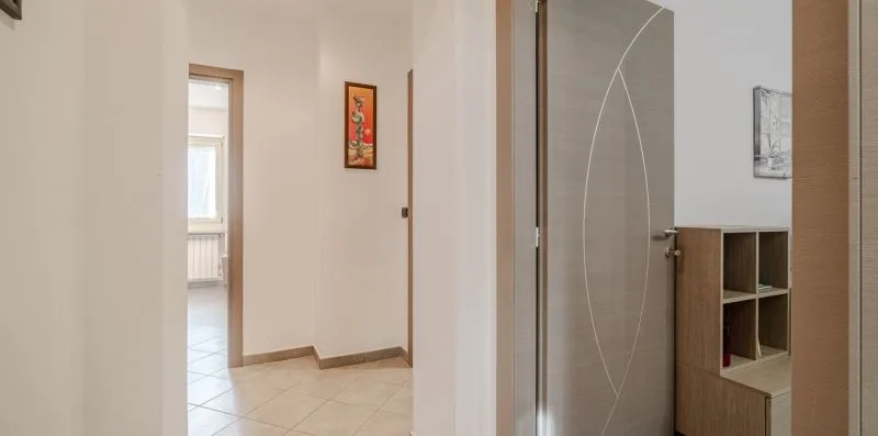 Un pasillo con suelo de baldosas, una puerta abierta y un armario de madera.
