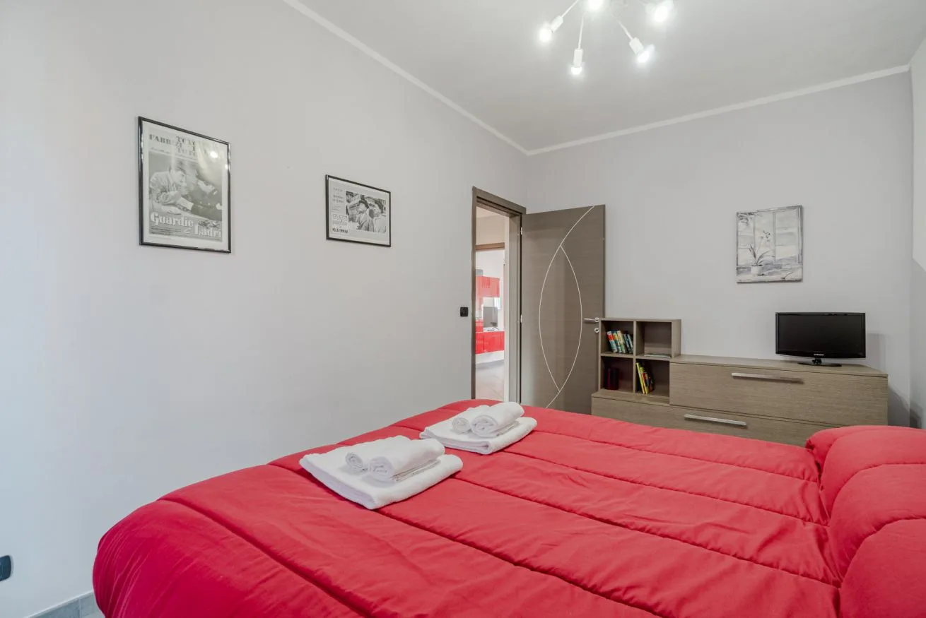 Un dormitorio con una colcha roja y un televisor sobre un mueble bajo.