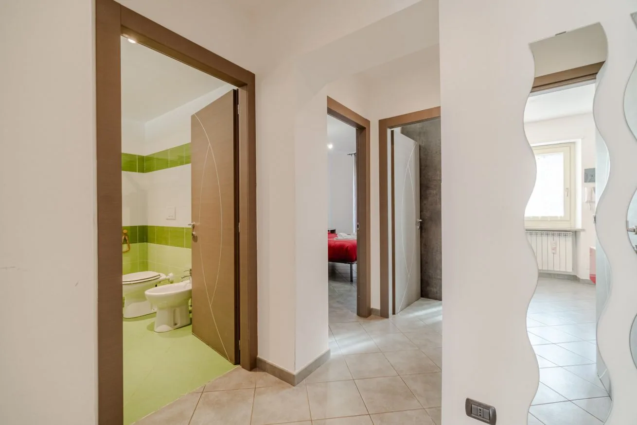 Un pasillo de baldosas con puertas abiertas y un espejo de pared.