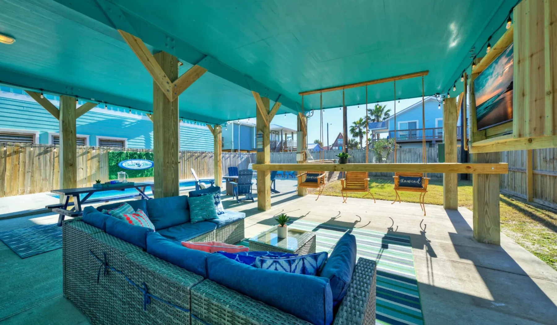 A covered outdoor lounge with cushioned seating and a long table.