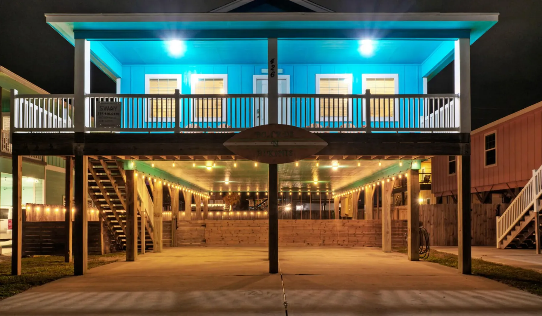 A raised two-story house glows at night above a covered patio.
