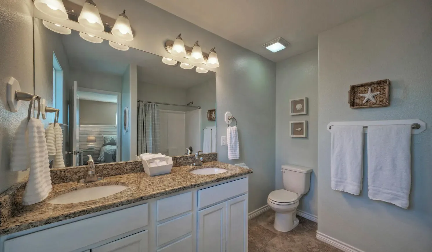 A bathroom vanity with a wide mirror, countertop sinks, and a toilet.