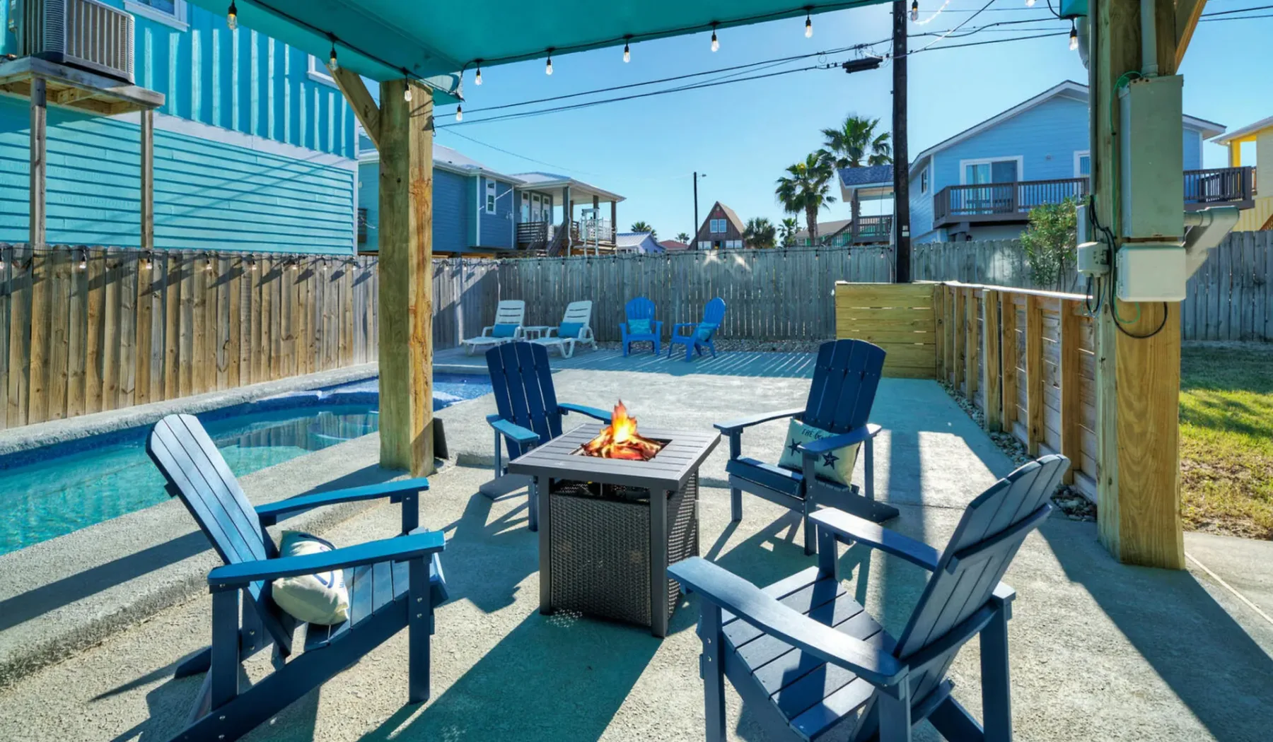 An outdoor patio seating area with a small fire table beneath a covered pergola.