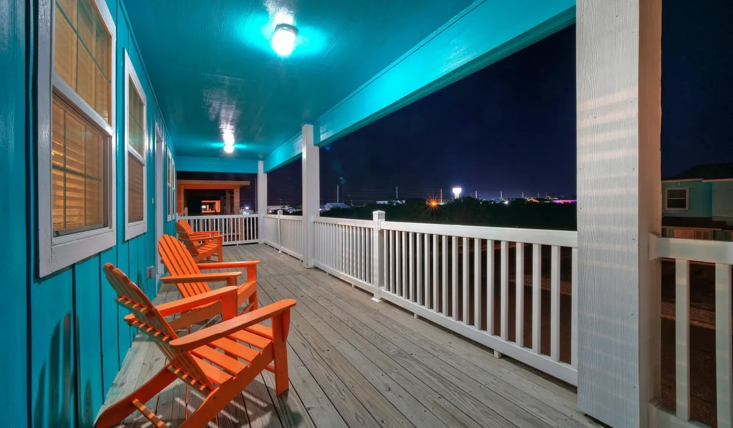 A covered porch at night with wooden seating and a white railing.