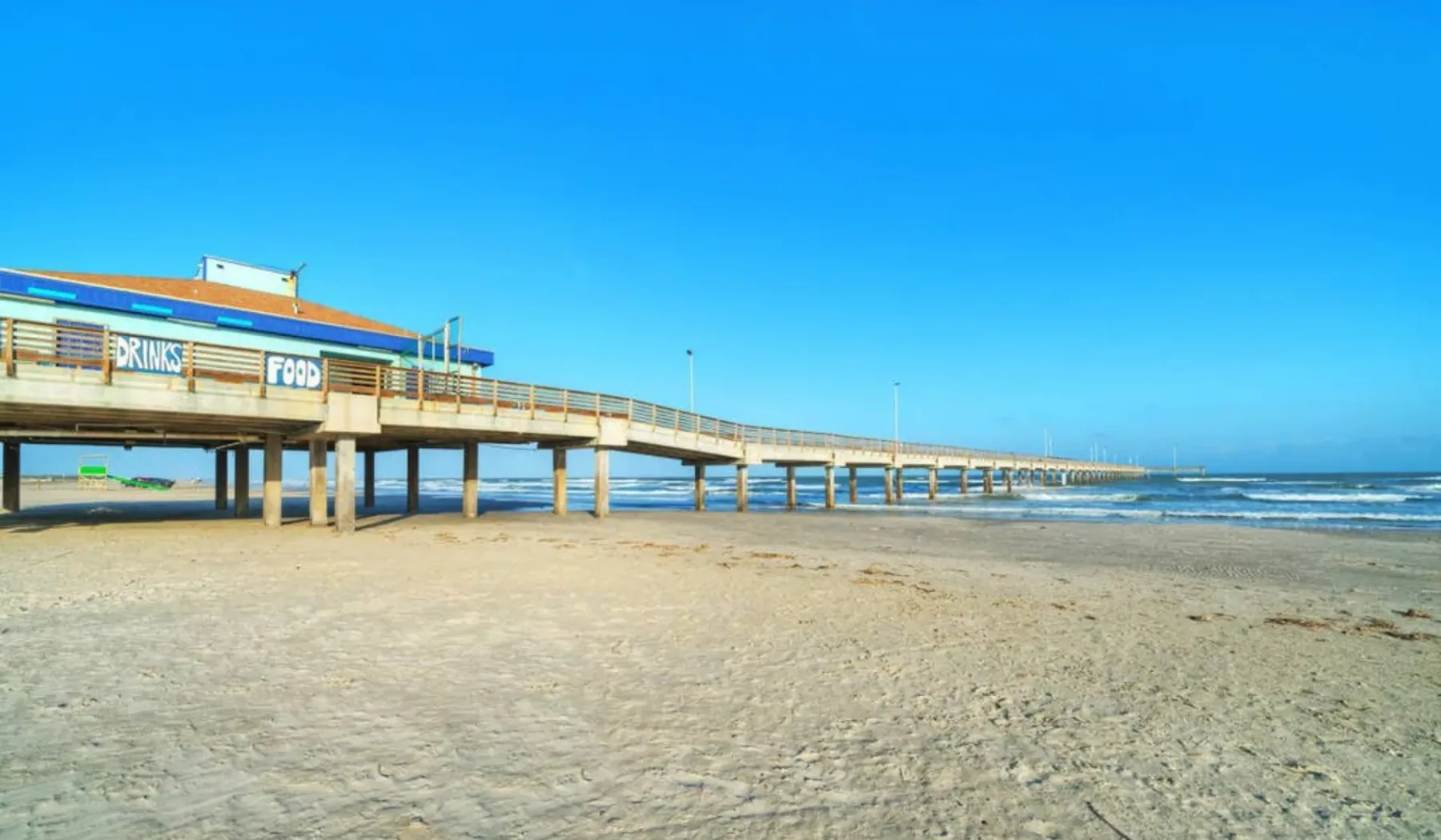 A long pier extends over a sandy beach beside the sea.