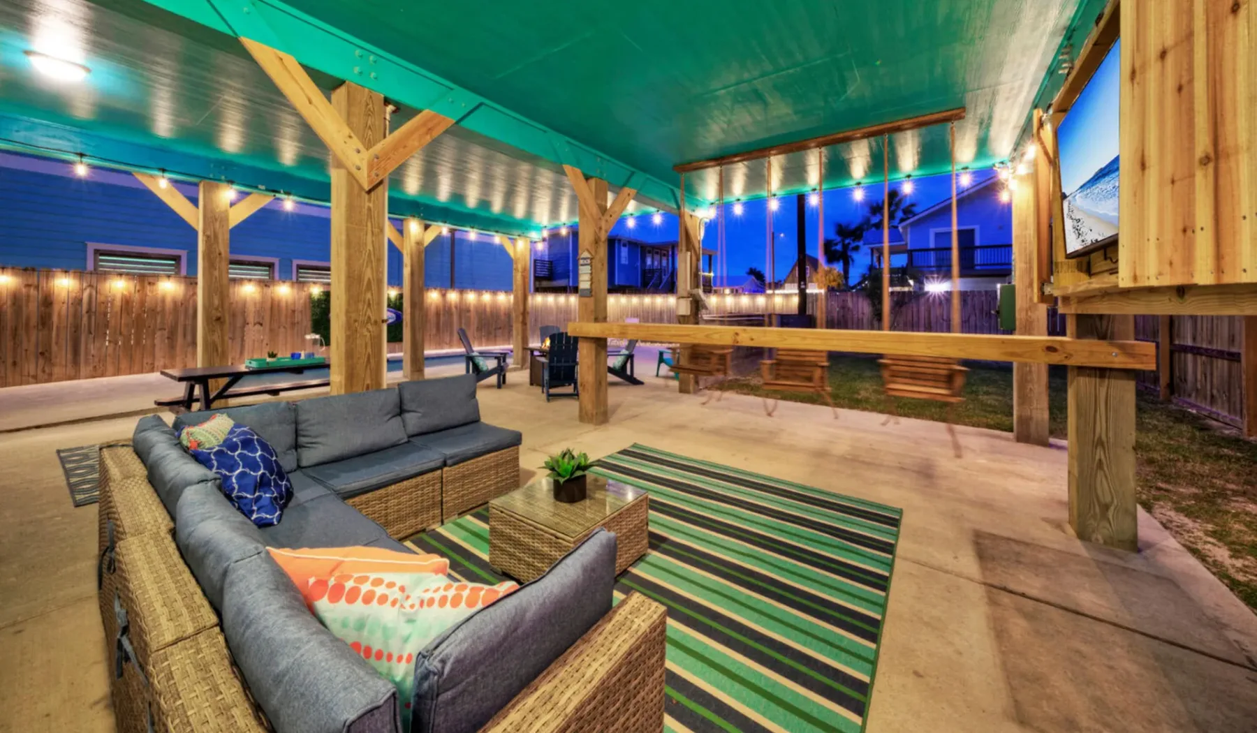 A covered outdoor lounge with seating around a striped rug and a long wooden counter.