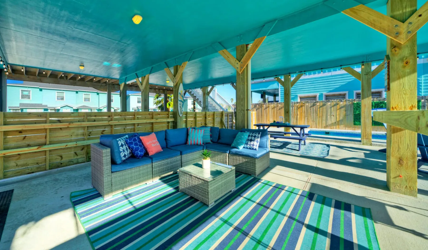 A covered outdoor seating area with a sectional sofa and striped rug.