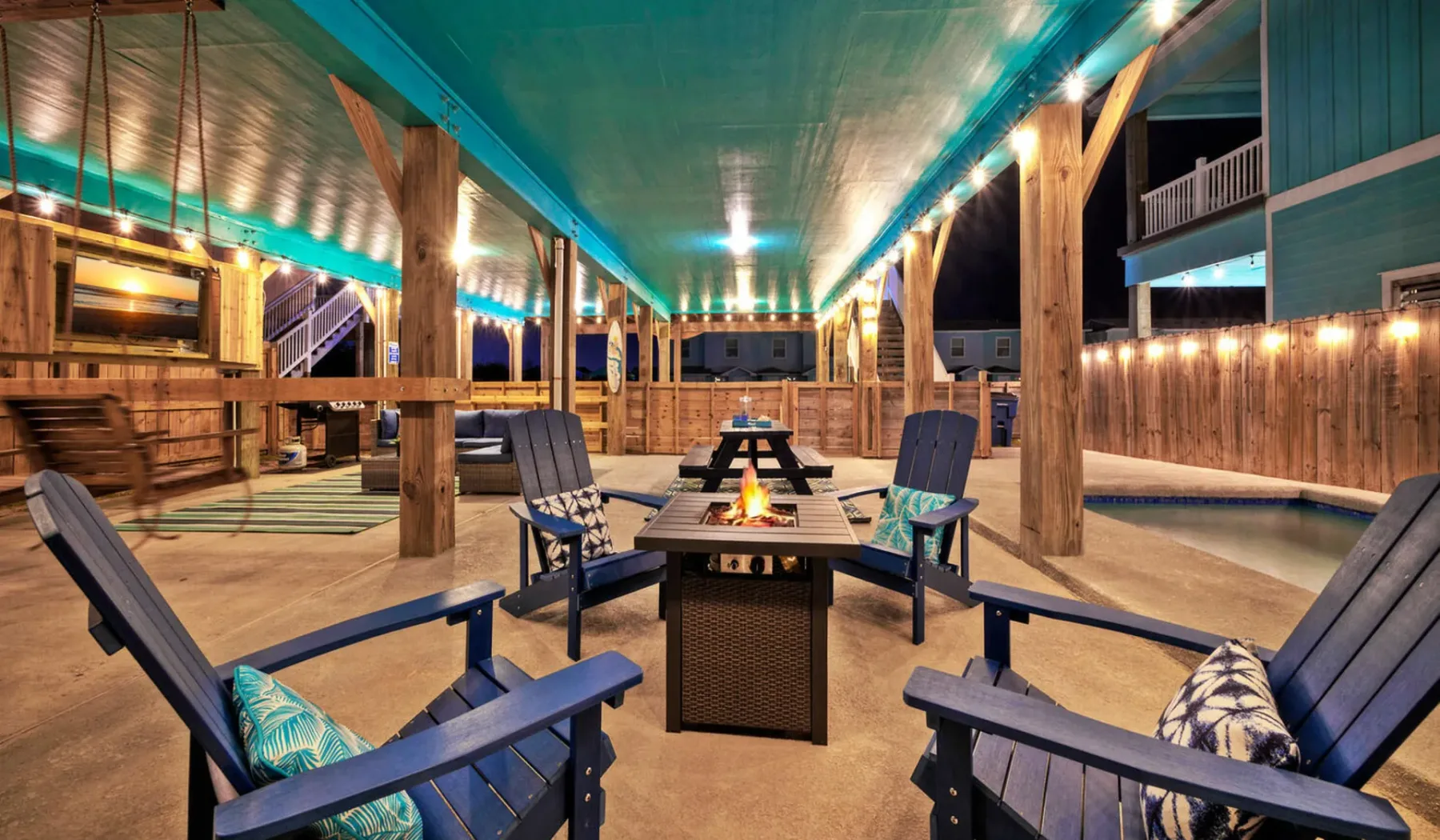 A covered outdoor seating area has a central table with a small fire feature.