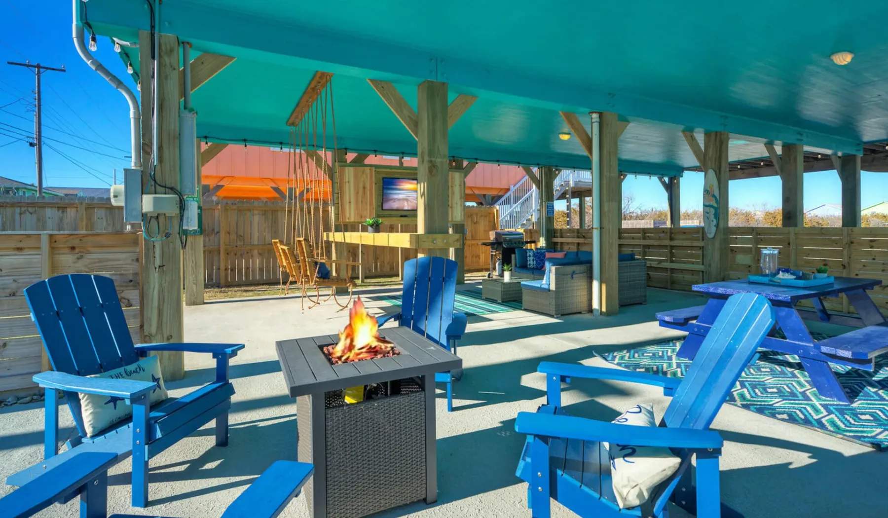 A covered outdoor seating area with blue chairs and a fire pit.