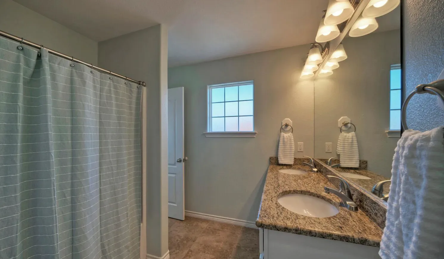 A bathroom with a long vanity, mirror, and curtained shower.