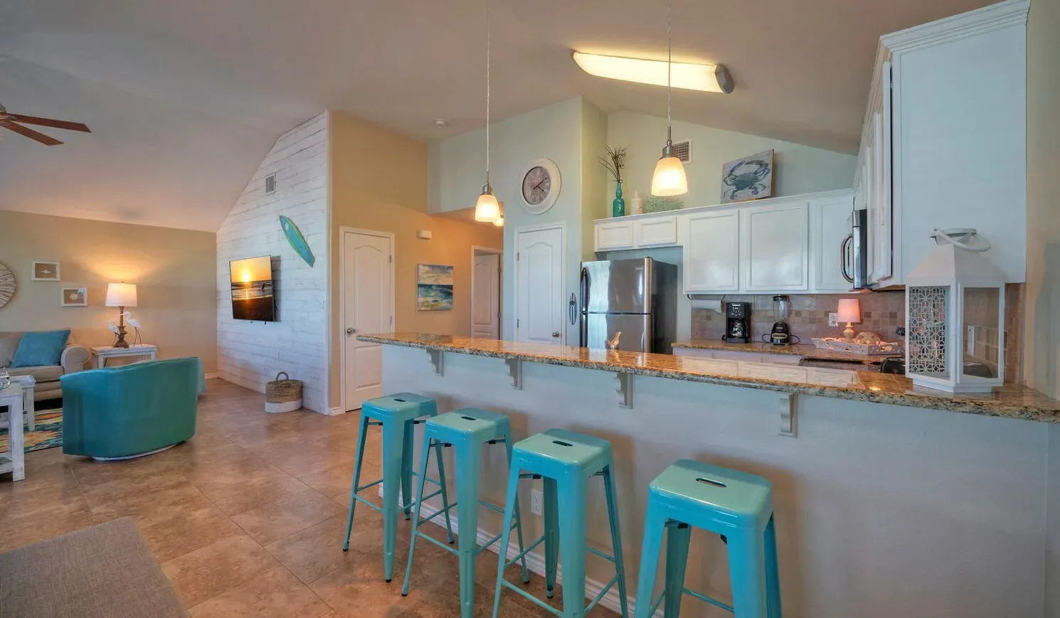 An open-plan living area and kitchen, with turquoise bar stools along the counter.