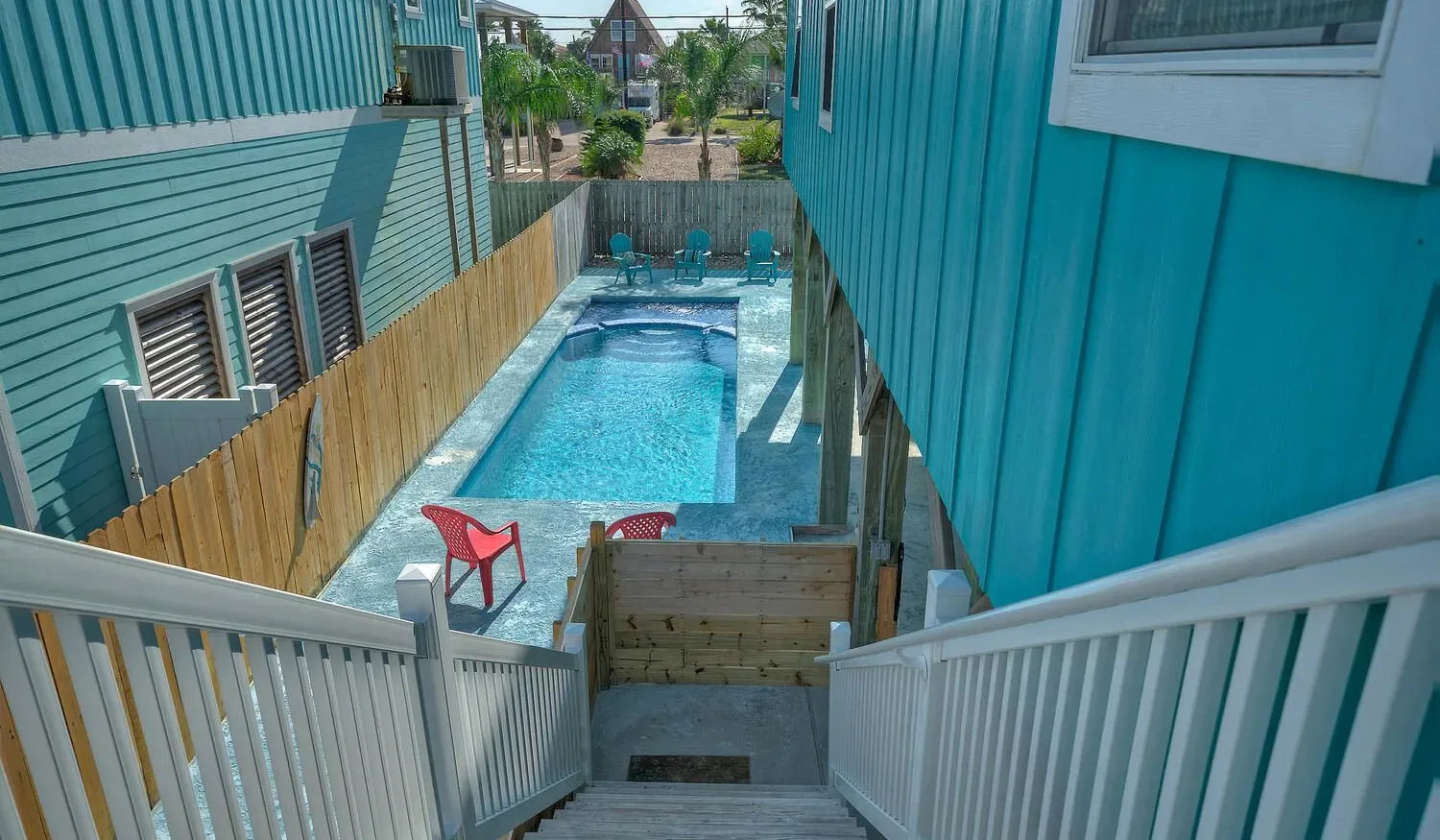 A narrow outdoor swimming pool sits between two turquoise-sided buildings.