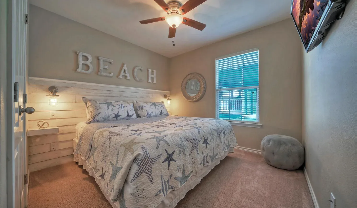 A bedroom with a bed, coastal-themed bedding, and a window with blue blinds.