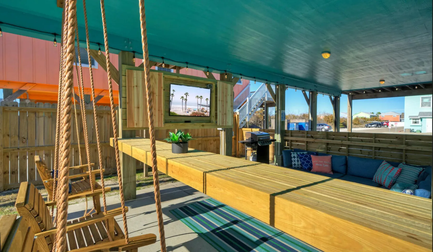 A covered outdoor lounge has built-in wooden seating and open window views.