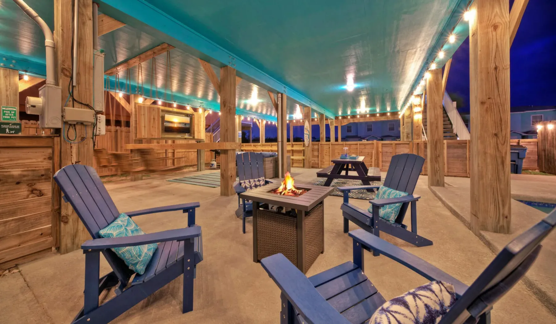A covered outdoor seating area with blue chairs and a small fire table.