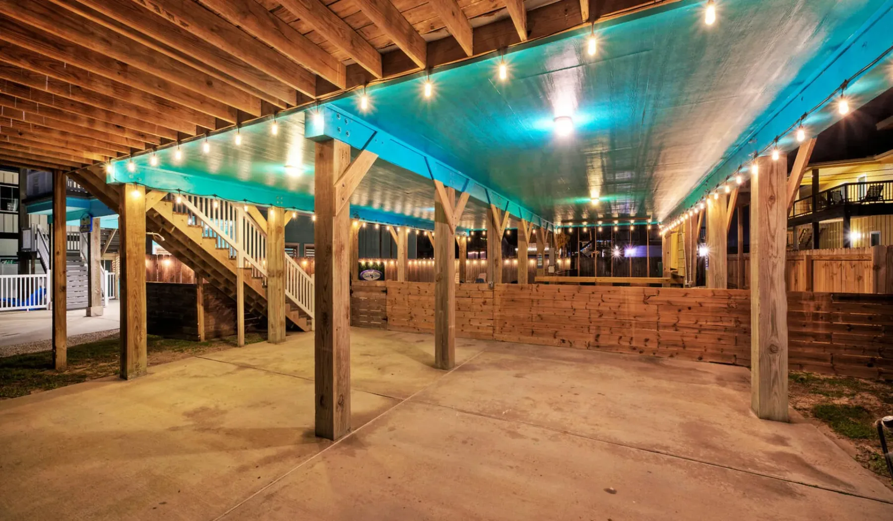 A covered outdoor patio with wooden posts, string lights, and a concrete floor.