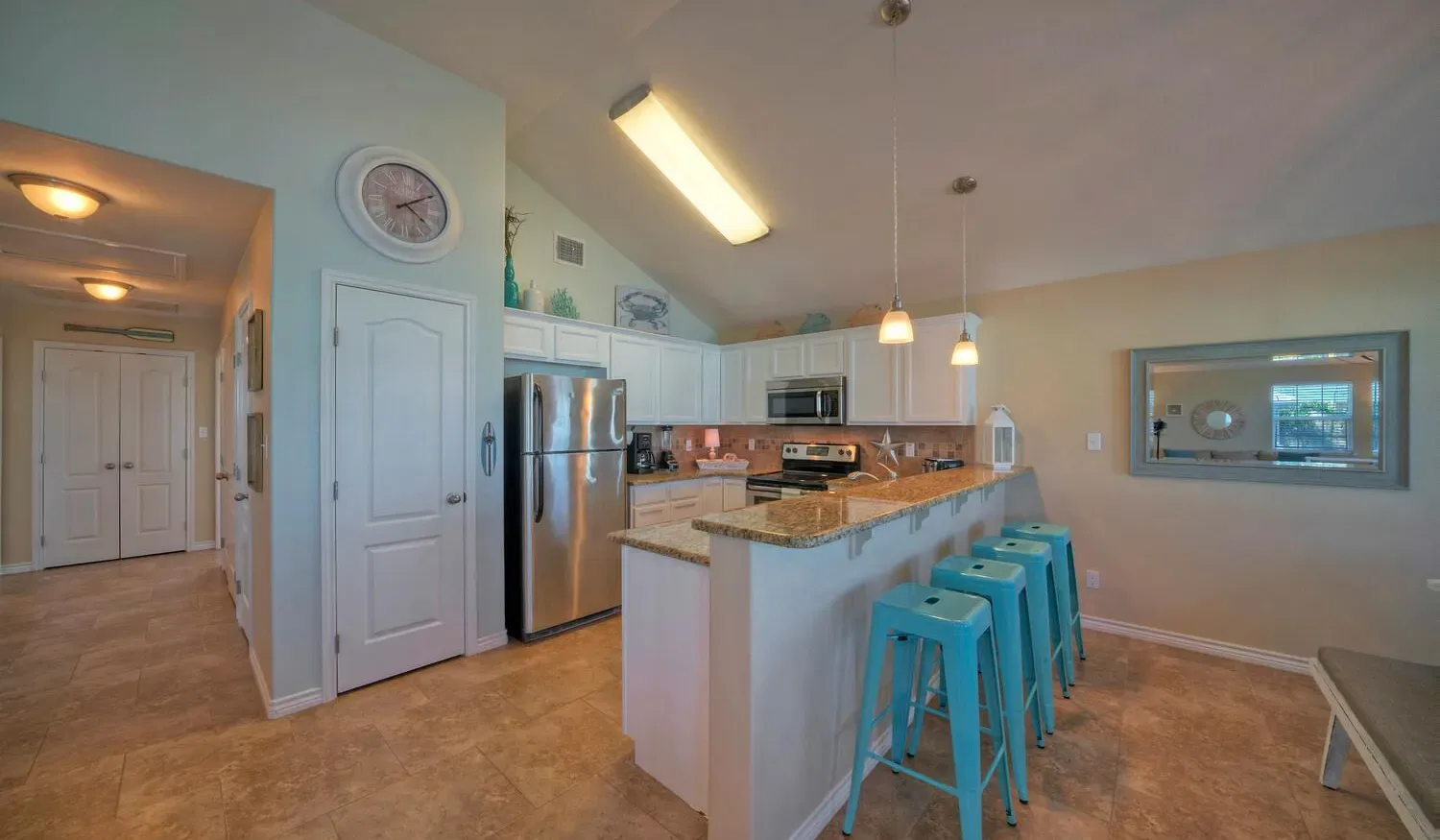A kitchen with a central counter, turquoise stools, and stainless steel appliances.
