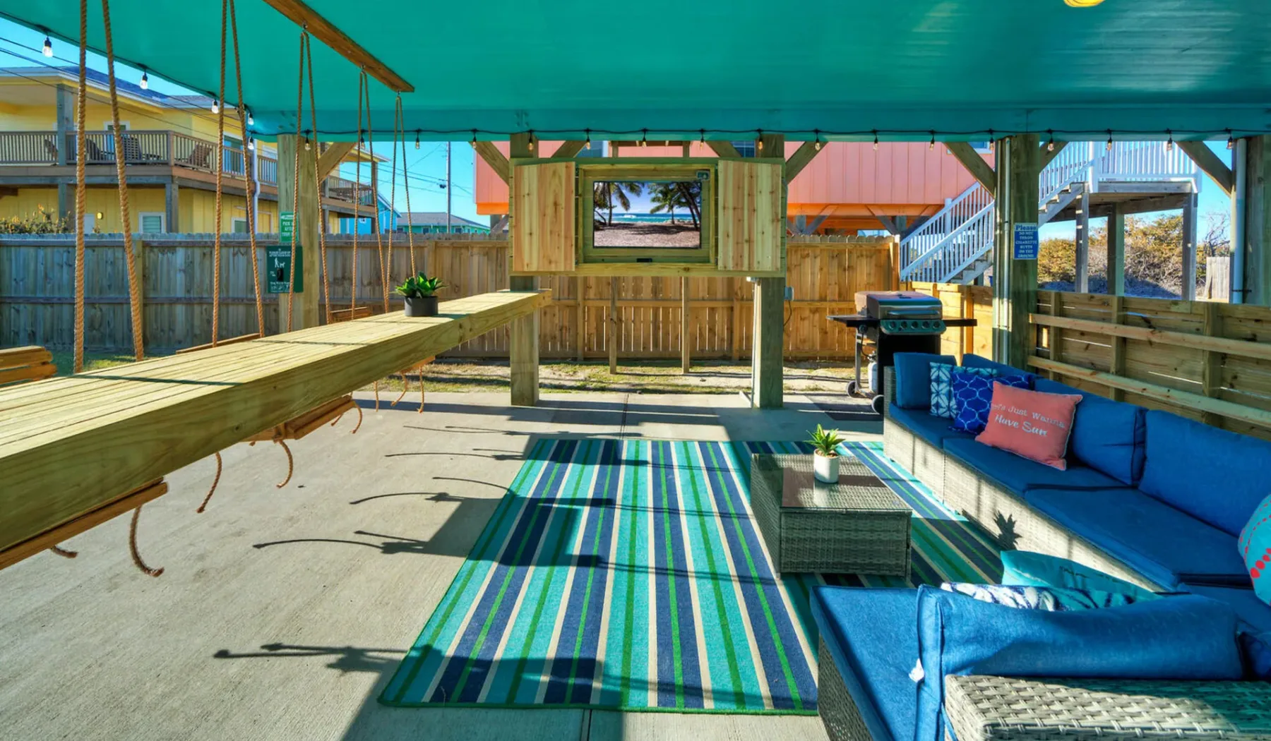 A covered outdoor seating area has blue cushions and a striped rug.