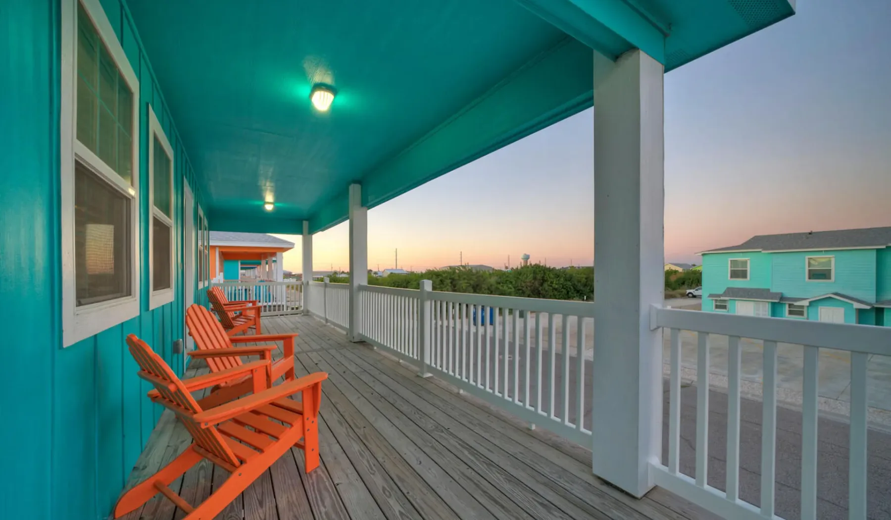 A covered porch with orange seating overlooks neighboring buildings at dusk.