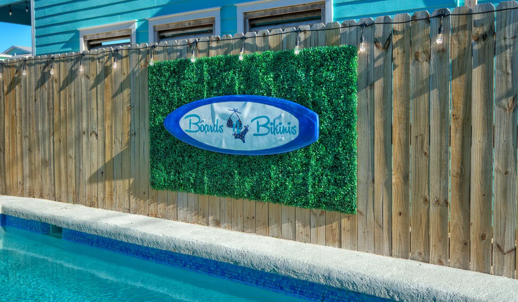 A swimming pool runs alongside a wooden fence with a green sign.