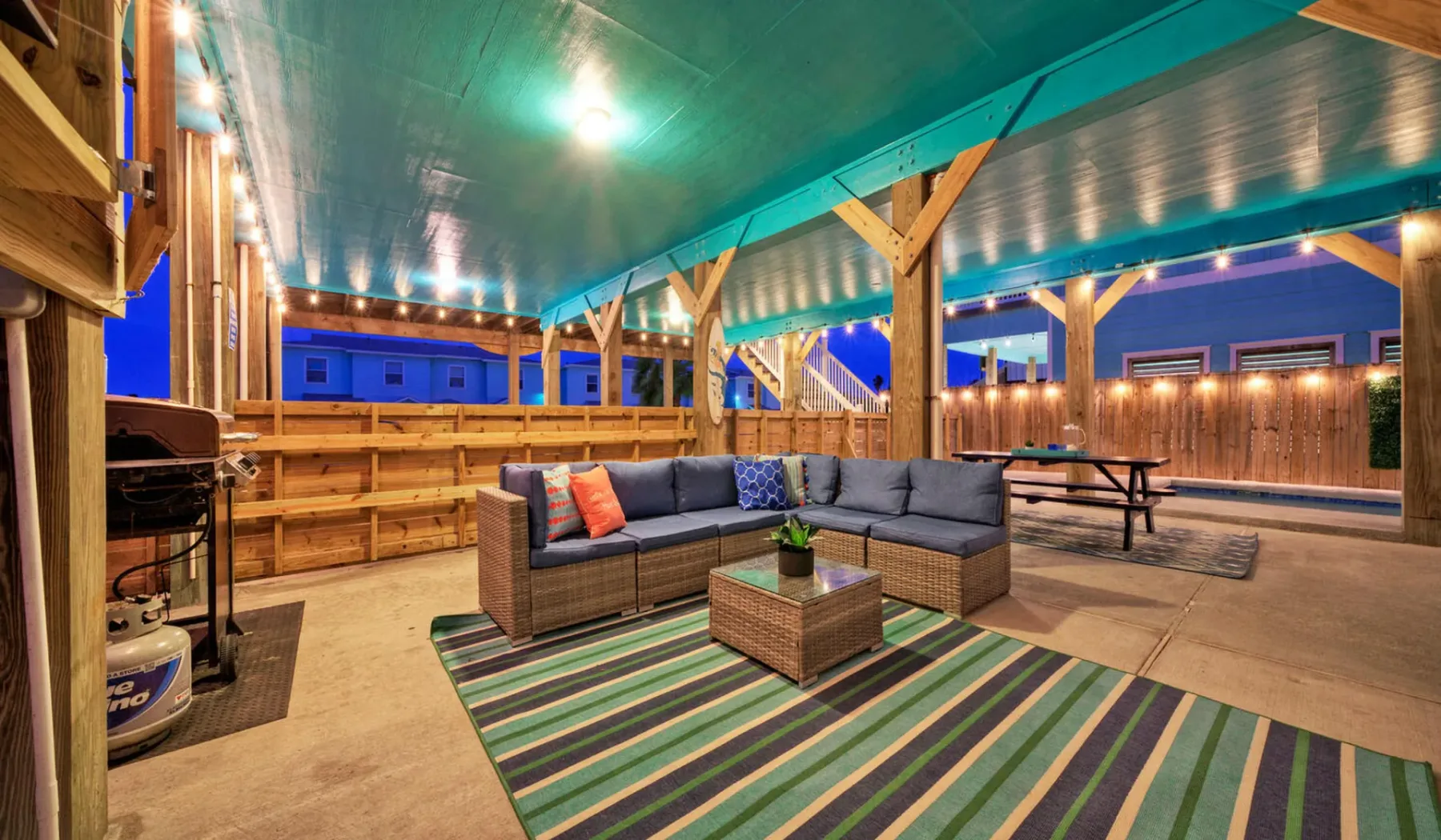 A covered outdoor lounge with sectional seating around a low table.