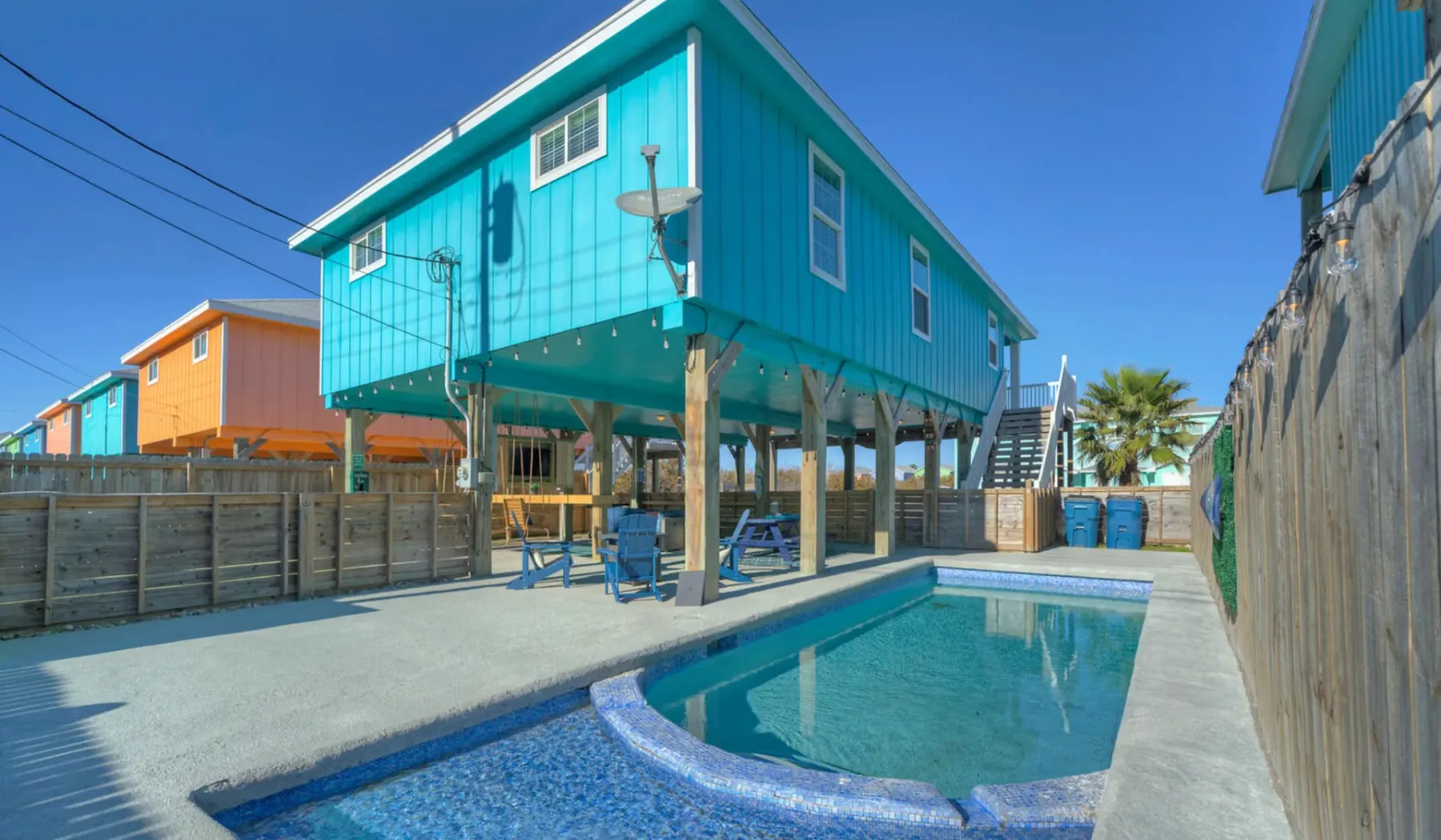 An outdoor pool sits beside a turquoise elevated building.