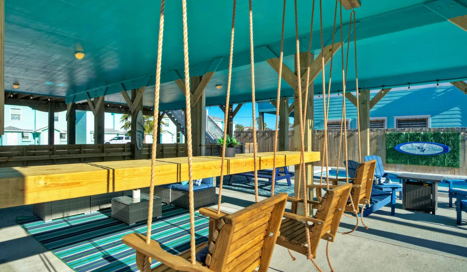A covered outdoor seating area features wooden swing seats and a long table.
