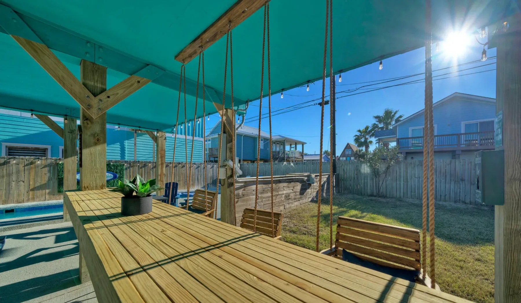 A covered wooden deck with hanging swings overlooks a fenced yard.