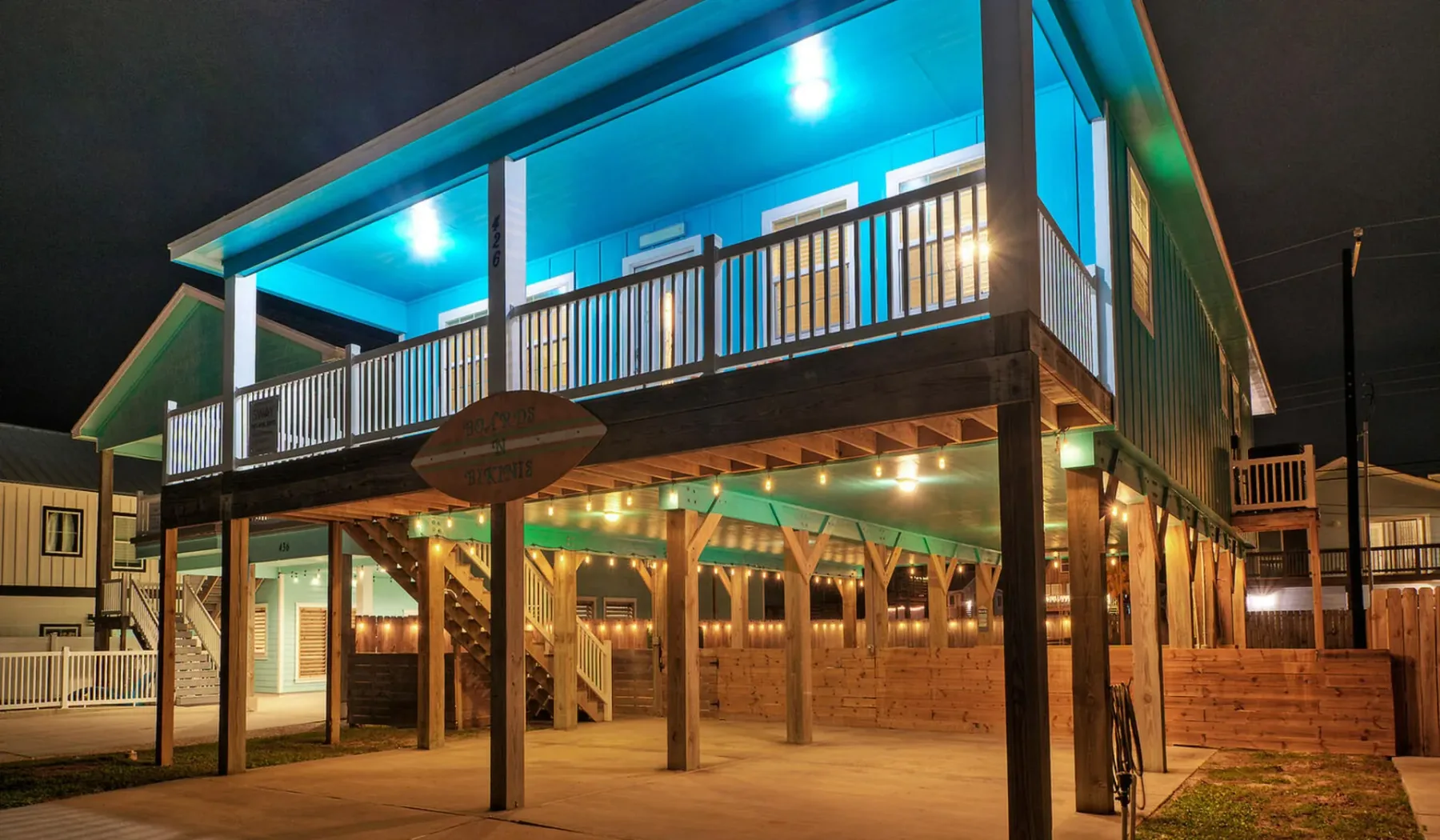 A raised wooden building at night has a brightly lit upper balcony.