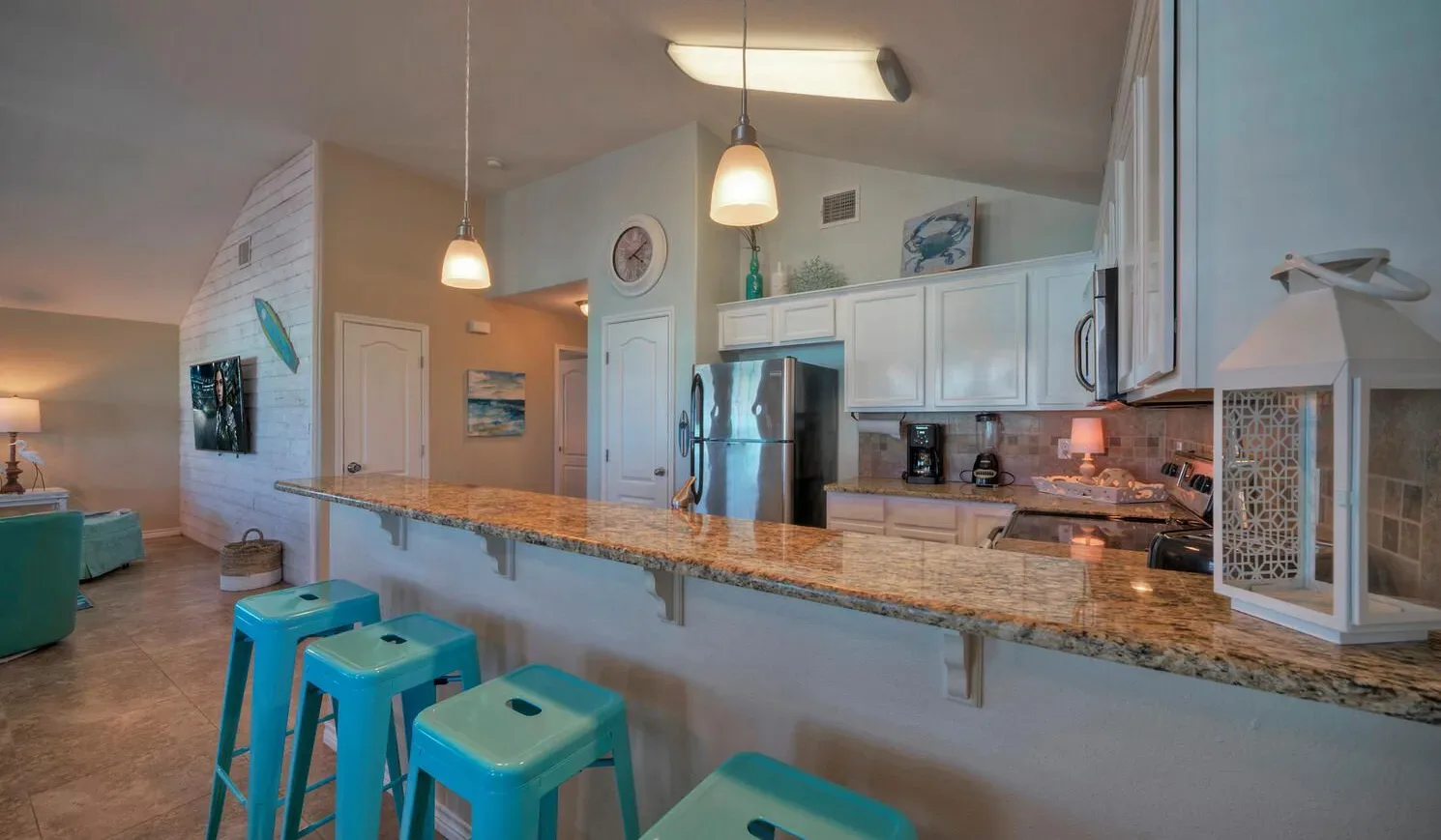 An open kitchen with a long breakfast bar and turquoise stools.