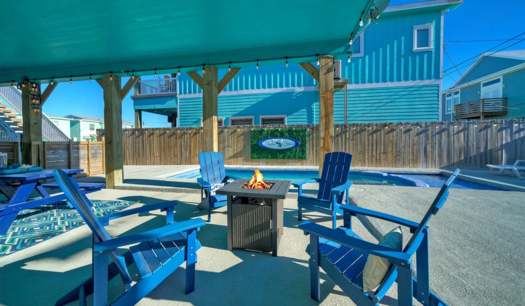 An outdoor seating area with blue chairs surrounds a small table beside a pool.