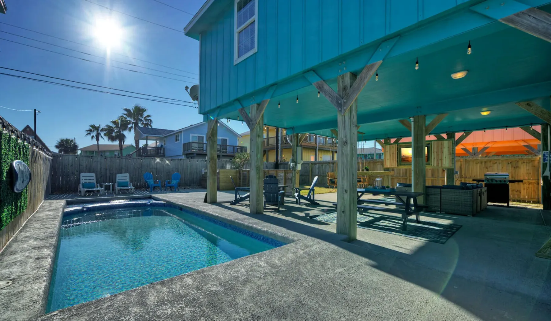 An outdoor swimming pool sits beside a covered patio with seating.