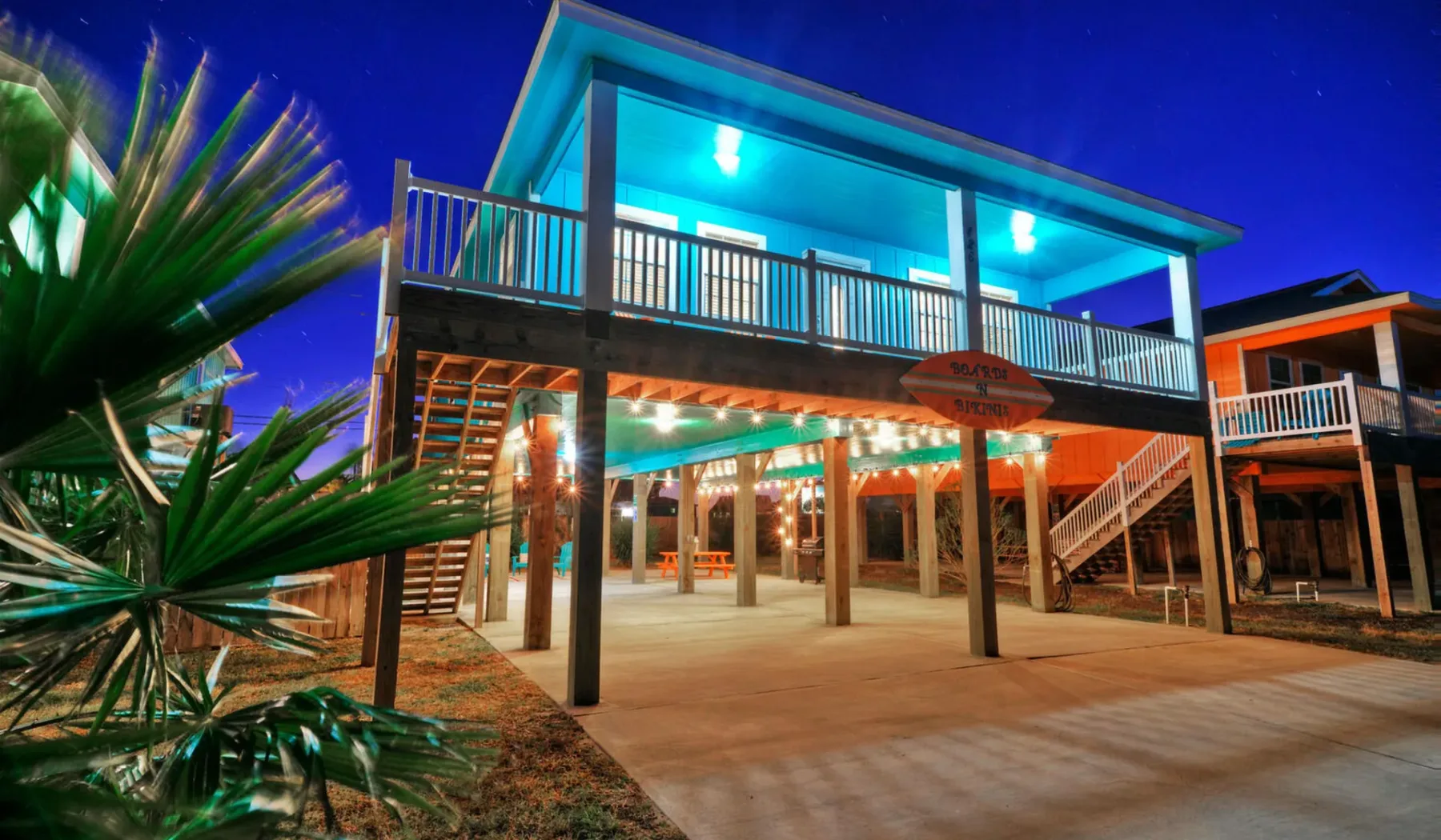 A brightly lit raised building at night, with a balcony above an open ground level.