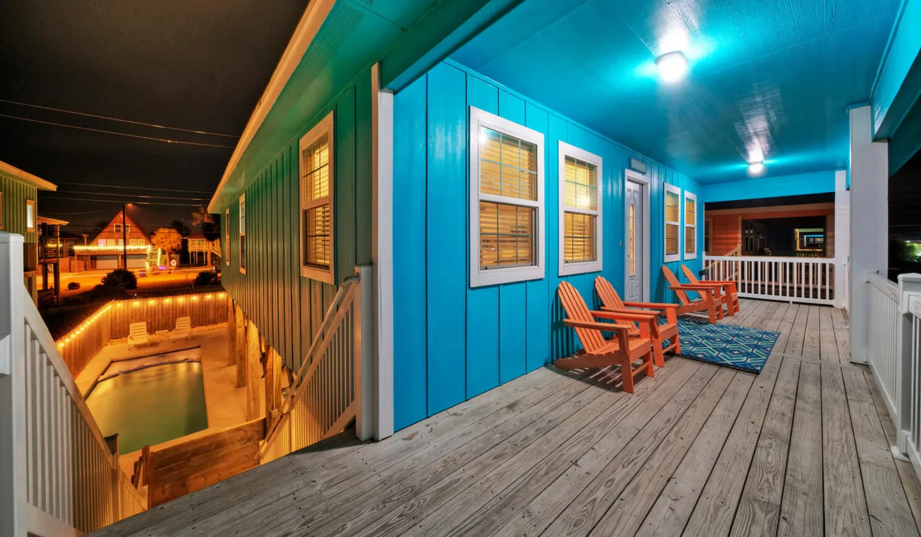 A covered porch with wooden seating overlooks a warmly lit outdoor pool.